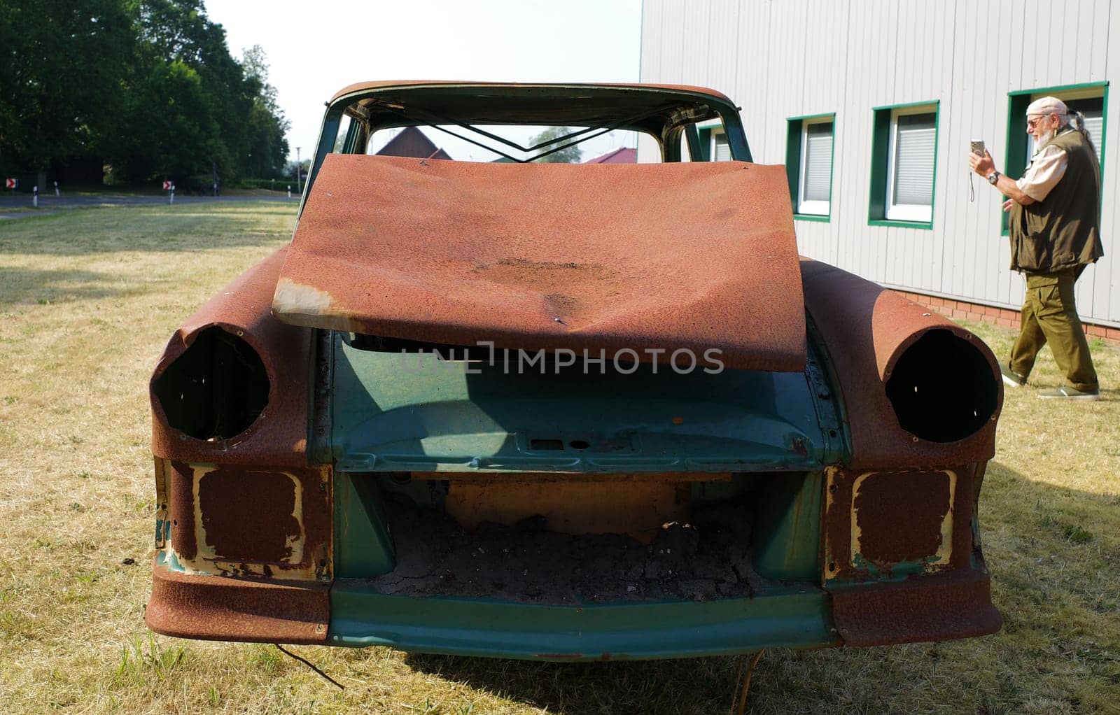 Front of a totally rusted old car with a man in the background photographing it