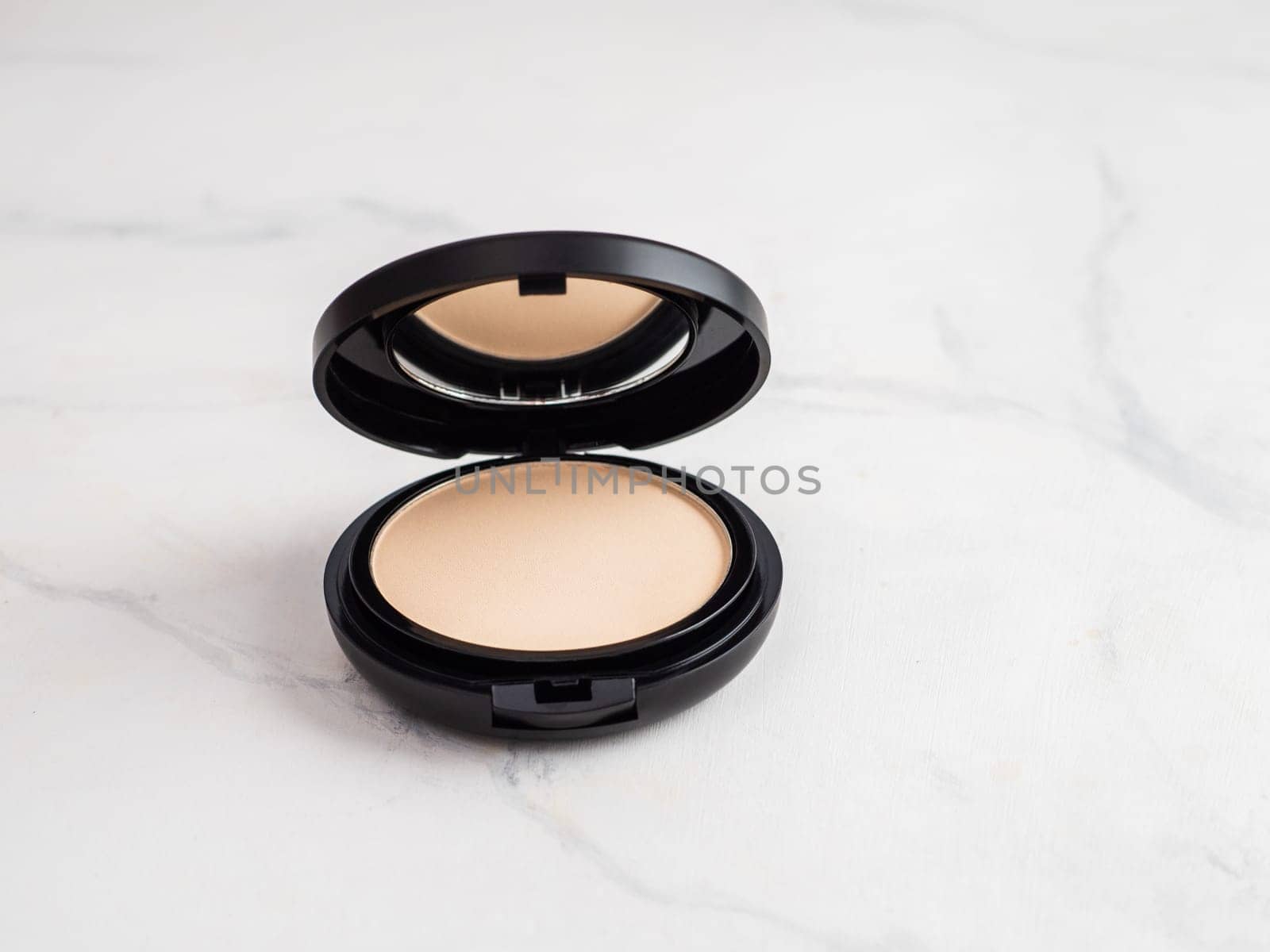 Compact powder on white marble background. Female pressed powder in opened black plastic case with mirror, copy space for text or design.