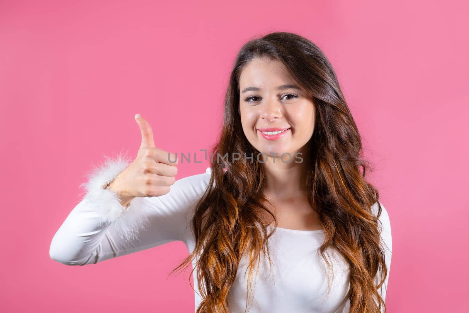 Portrait of brunette female student with a broad smile and showing thumbs up on the pink background