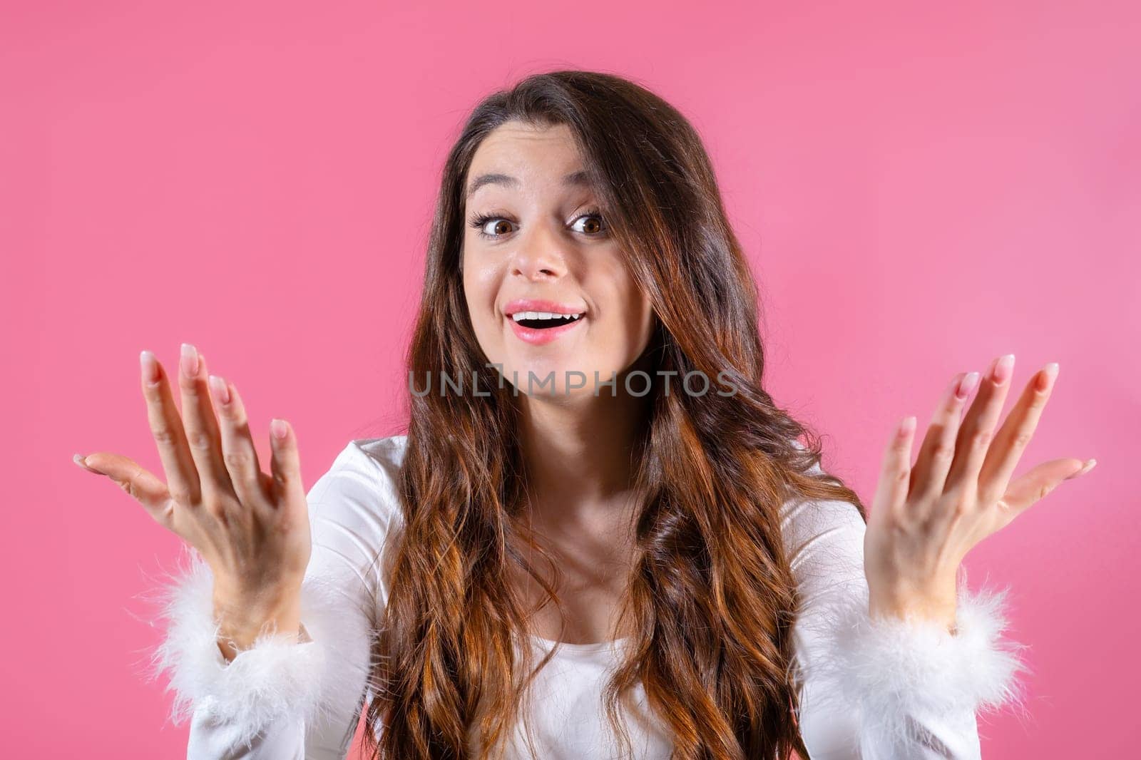 Portrait of a cheerful young woman happily gesturing with her hands on the pink background