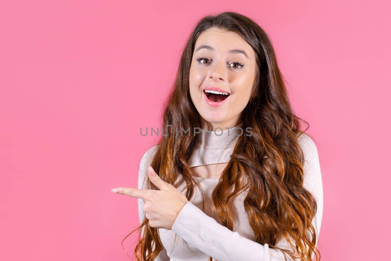 A portrait of a young student pointed by finger on copy space with pink background.