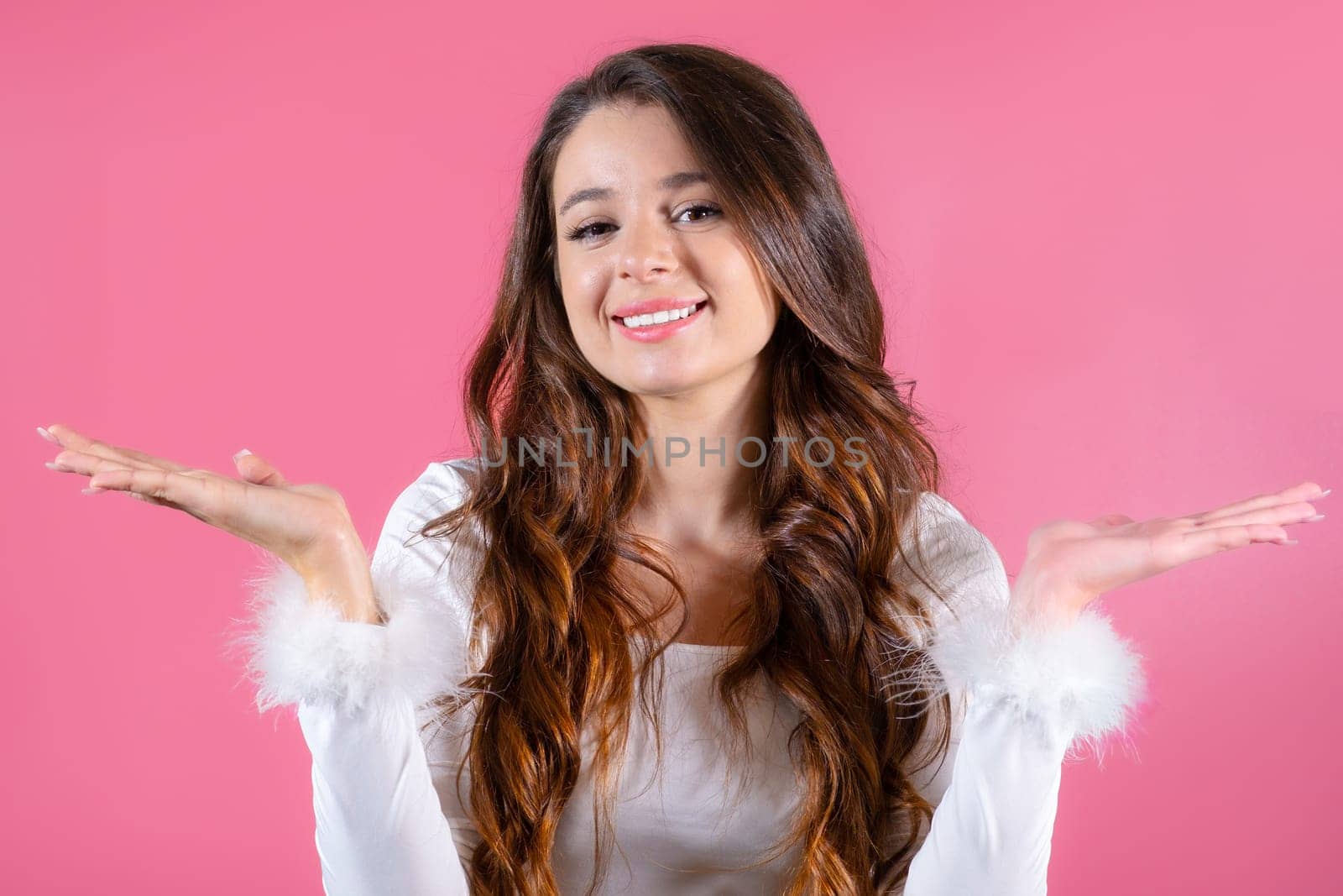 Portrait of a cheerful young lady happily gesturing with her hands on the pink background