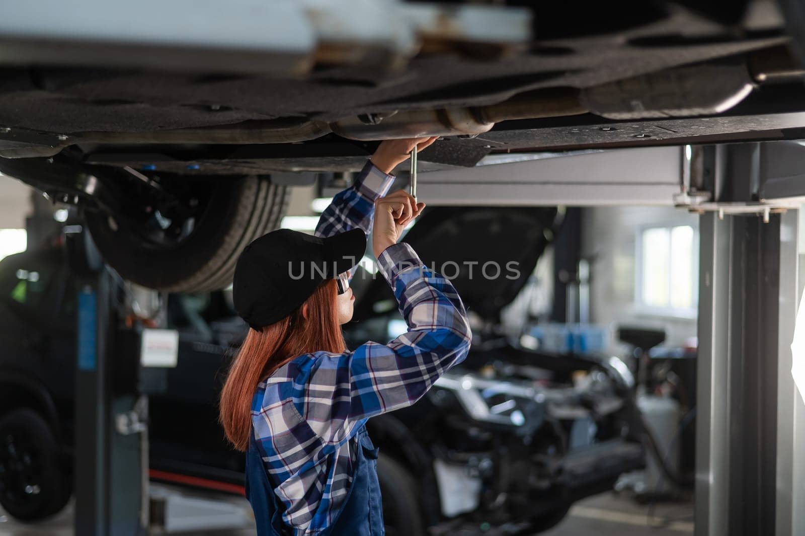 Female mechanic unscrew the nuts on the bottom of the car that is on the lift. A girl at a man's work