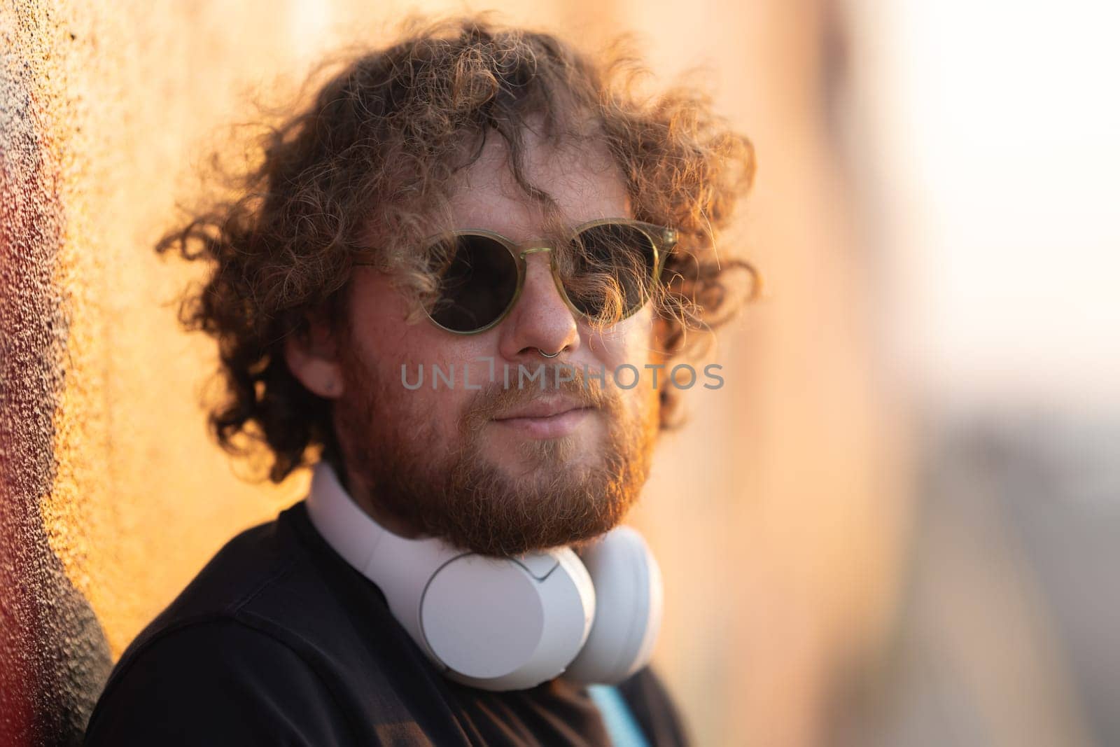 Romantic man with curly hair wearing wireless headphones at sunset. Portrait