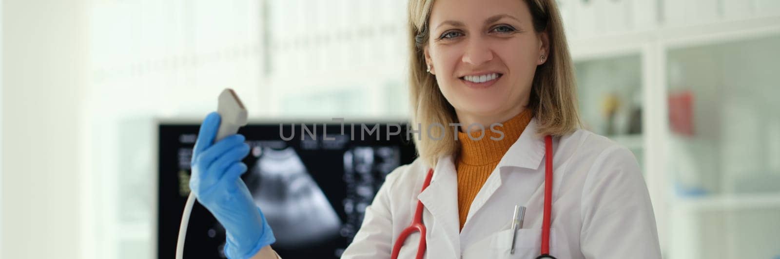 Smiling woman doctor holding ultrasound probe in hands to diagnose early pregnancy in clinic. Medical insurance concept