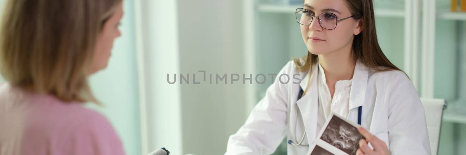 Doctor communicating with patient and examining results of ultrasound examination of internal organs in clinic. Ultrasound diagnosis of pregnancy concept