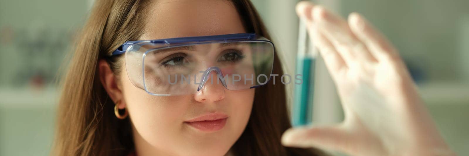 Woman scientist chemist looking at test tube with blue liquid in chemistry lab. Biochemistry concept