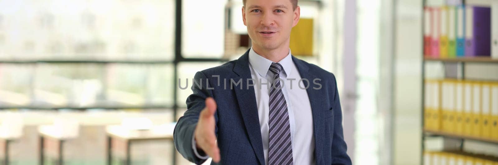 Smiling businessman extending hand for handshake with client in office. Working together with partners concept