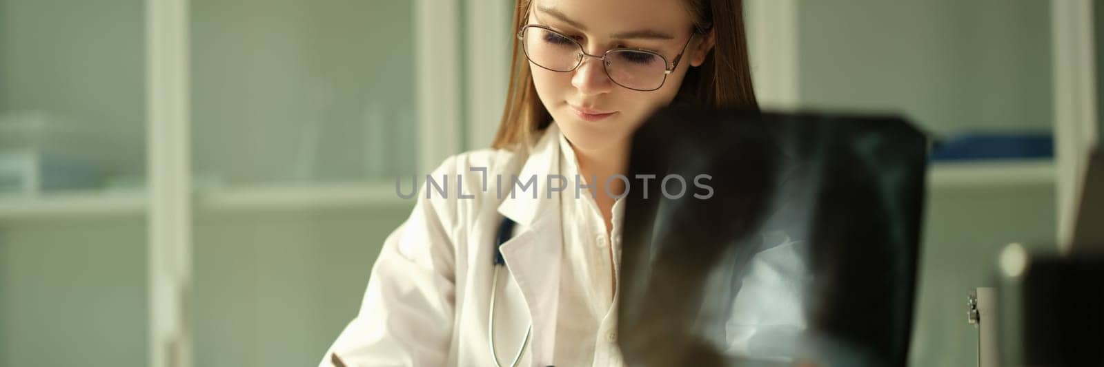 Doctor pulmonologist examining x-ray lungs and writing patient medical history in clinic by kuprevich
