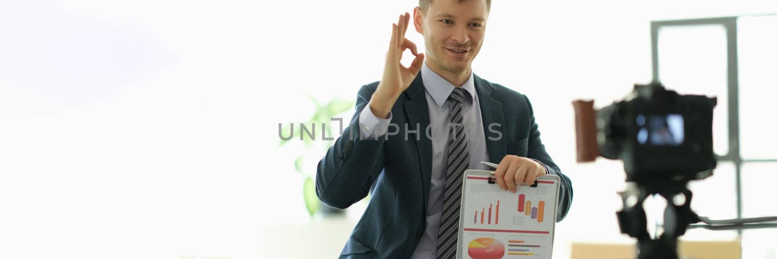 Business coach man showing ok gesture and holding papers with charts in front of camera. Online video conferencing concept