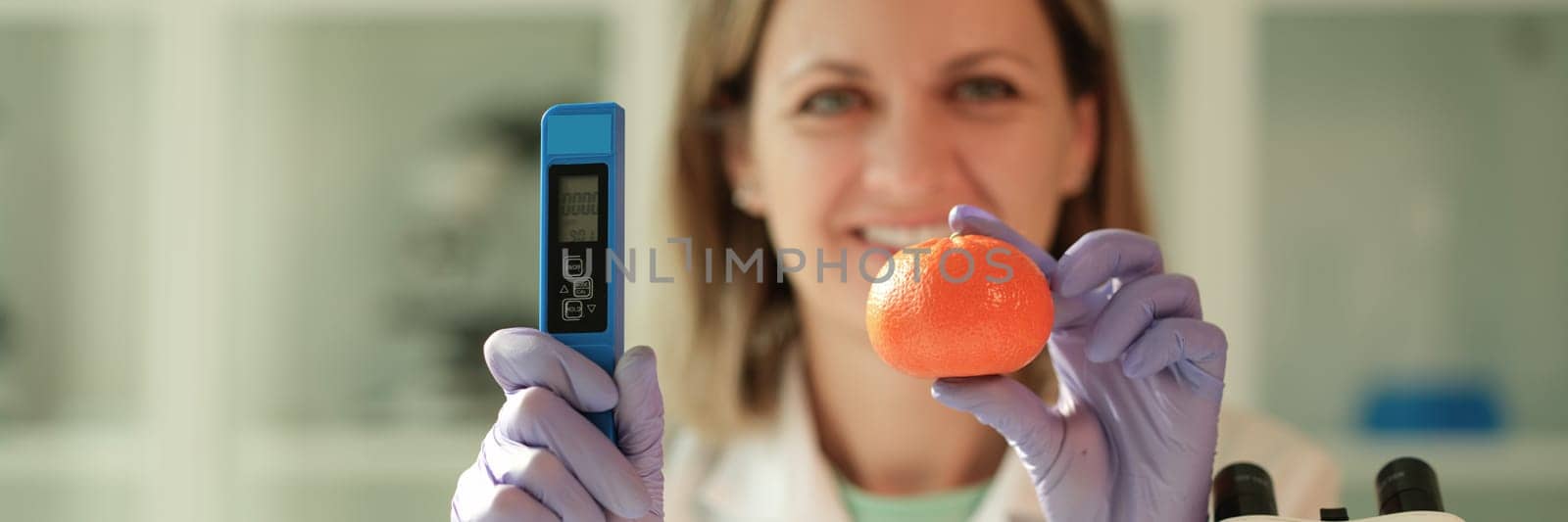 Scientist chemist holding in hands tangerine and device for measuring amount of nitrates in chemical laboratory closeup by kuprevich