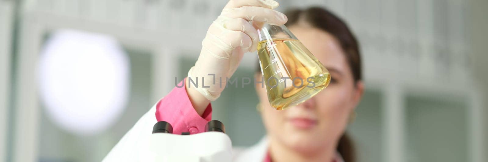 Scientist chemist looking at flask with yellow liquid or oil for transparency in chemical laboratory closeup by kuprevich