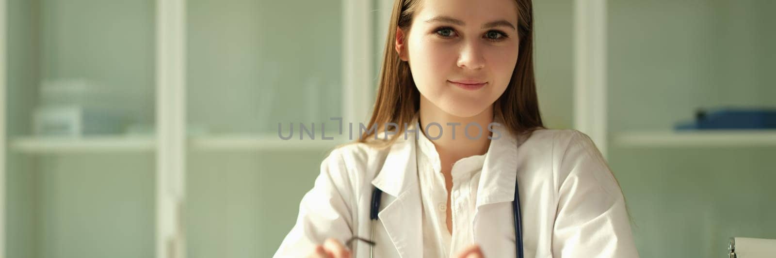 Portrait of young woman doctor with glasses in her hands in clinic by kuprevich
