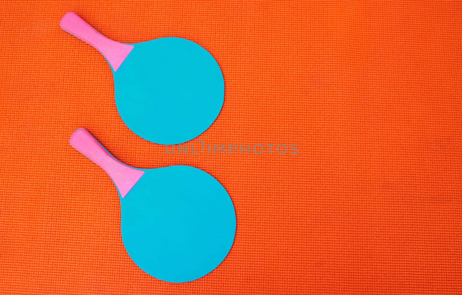 I need a partner. High angle shot of two table tennis bats placed together on top of an orange background inside of a studio