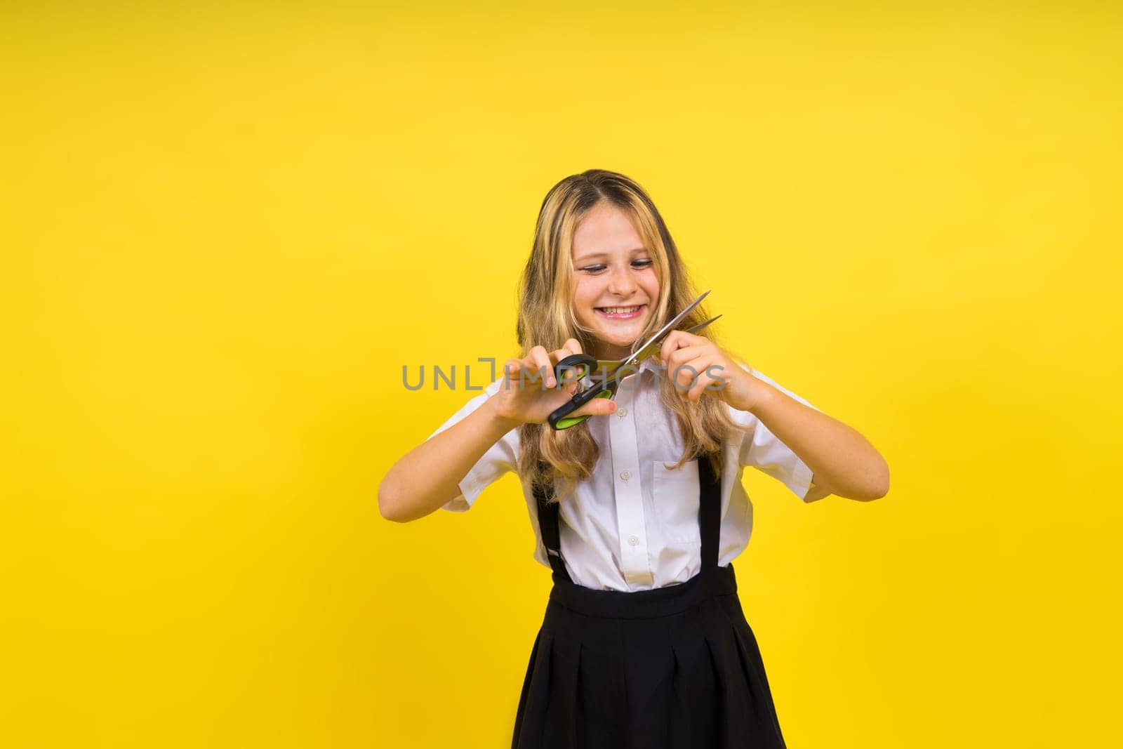 A young girl about to cut her own hair with a pair of scissors, isolated against yellow background by Zelenin