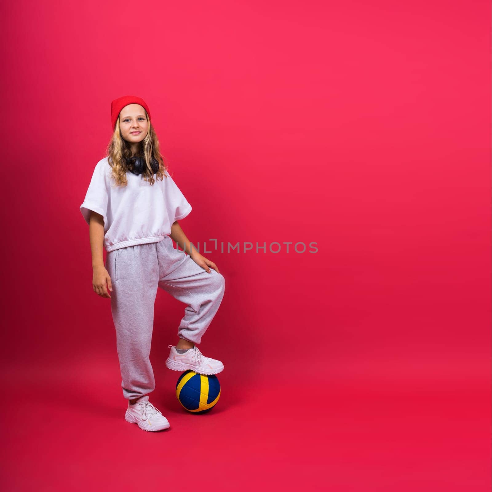 A teenager girl holds volleyball ball in hand and smiles on red yellow background. Studio photo.