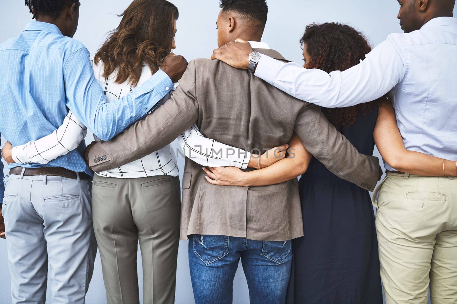 Strong teams have each others backs. Rearview studio shot of a group of businesspeople embracing against a gray background