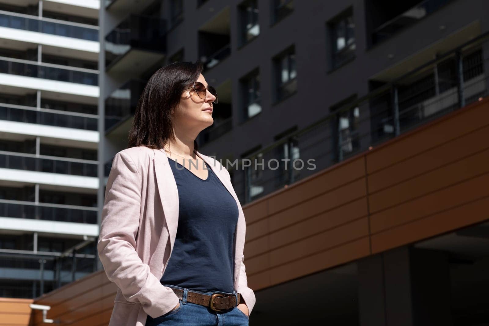 Happy Quadragenarian Woman Enjoys View Of New Apartment Campus, Complex At Day Time. Stylish Female Brunette Looks At Construction, Modern Residential Building, Horizontal Plane Lifestyle.