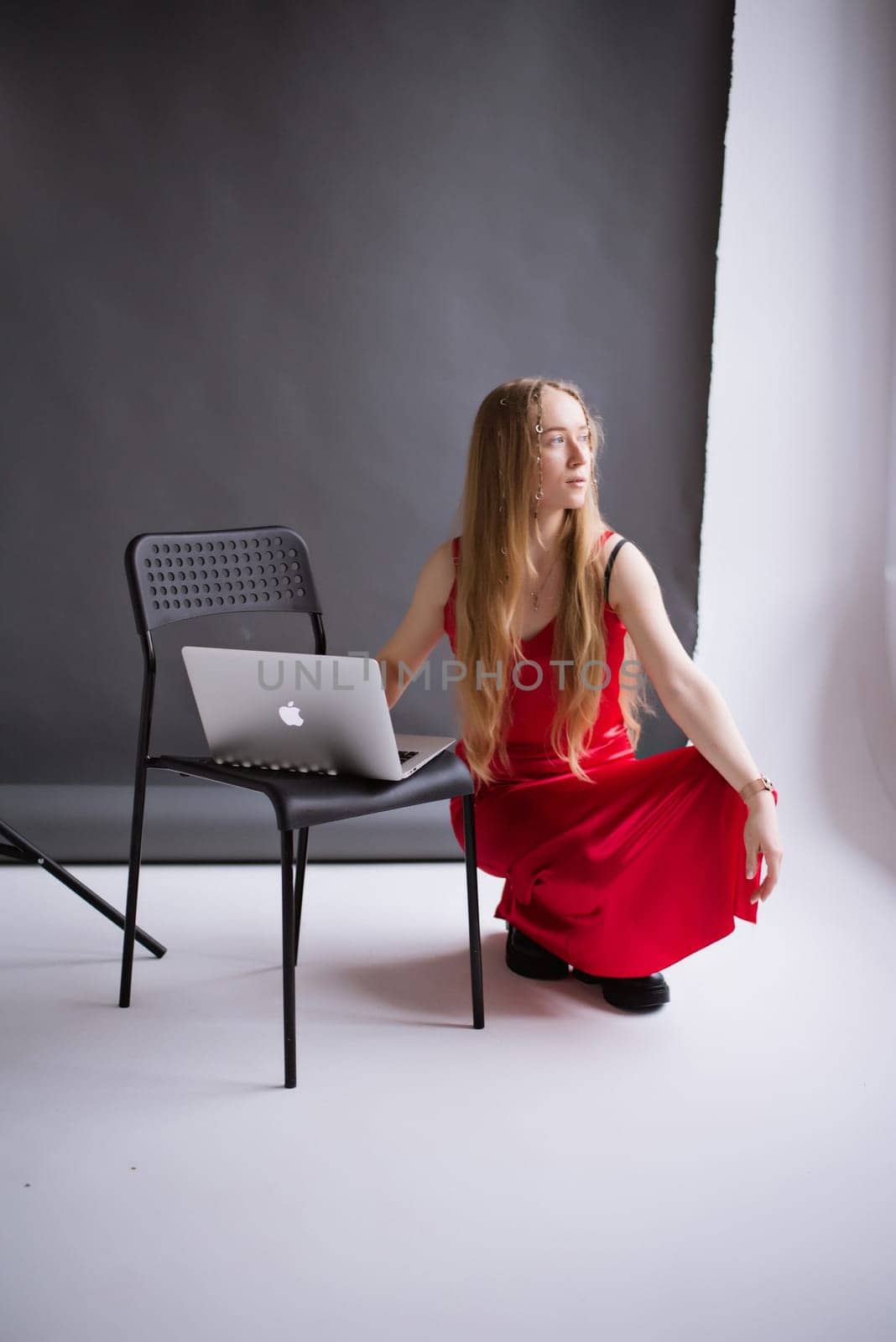 A business woman, lady blogger in a silk red dress is working, typing on a laptop apple . portrait blonde assistant of hands with computer MacBook, studio video production . Vertical