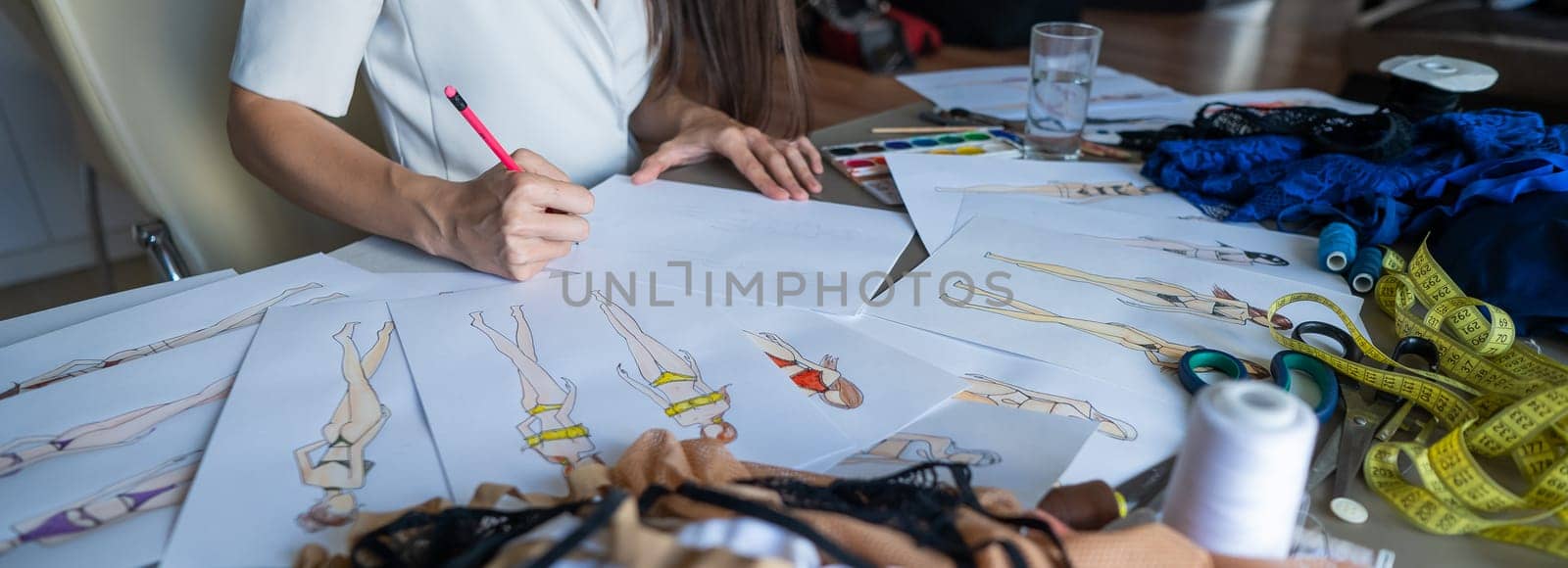 Faceless woman draws sketches of swimwear with a pencil. Close-up of the hands of a fashion designer