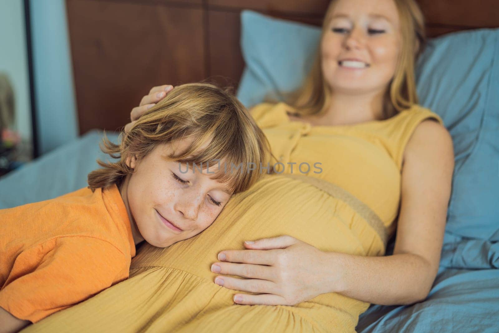 Young pregnant mother hugging her little boy lying in bed at night. Caring and loving parent hugging child.
