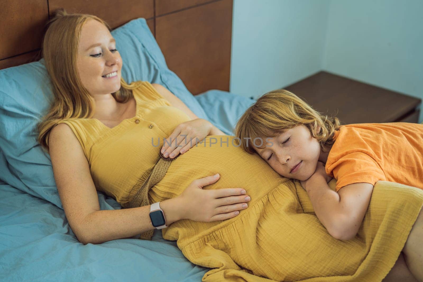 Young pregnant mother hugging her little boy lying in bed at night. Caring and loving parent hugging child.