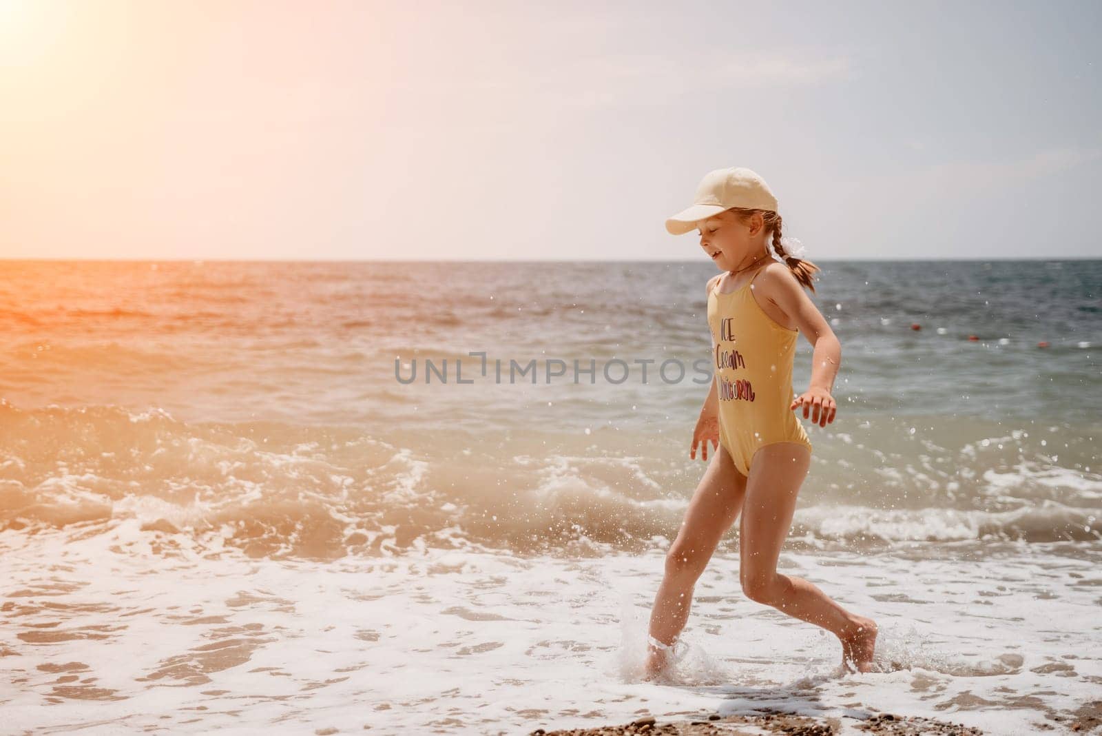 Cute little girl running along the seashore against a clear blue sea and rejoices in the rays of the summer sun. Beautiful girl in yellow swimsuit running and having fun on tropical beach