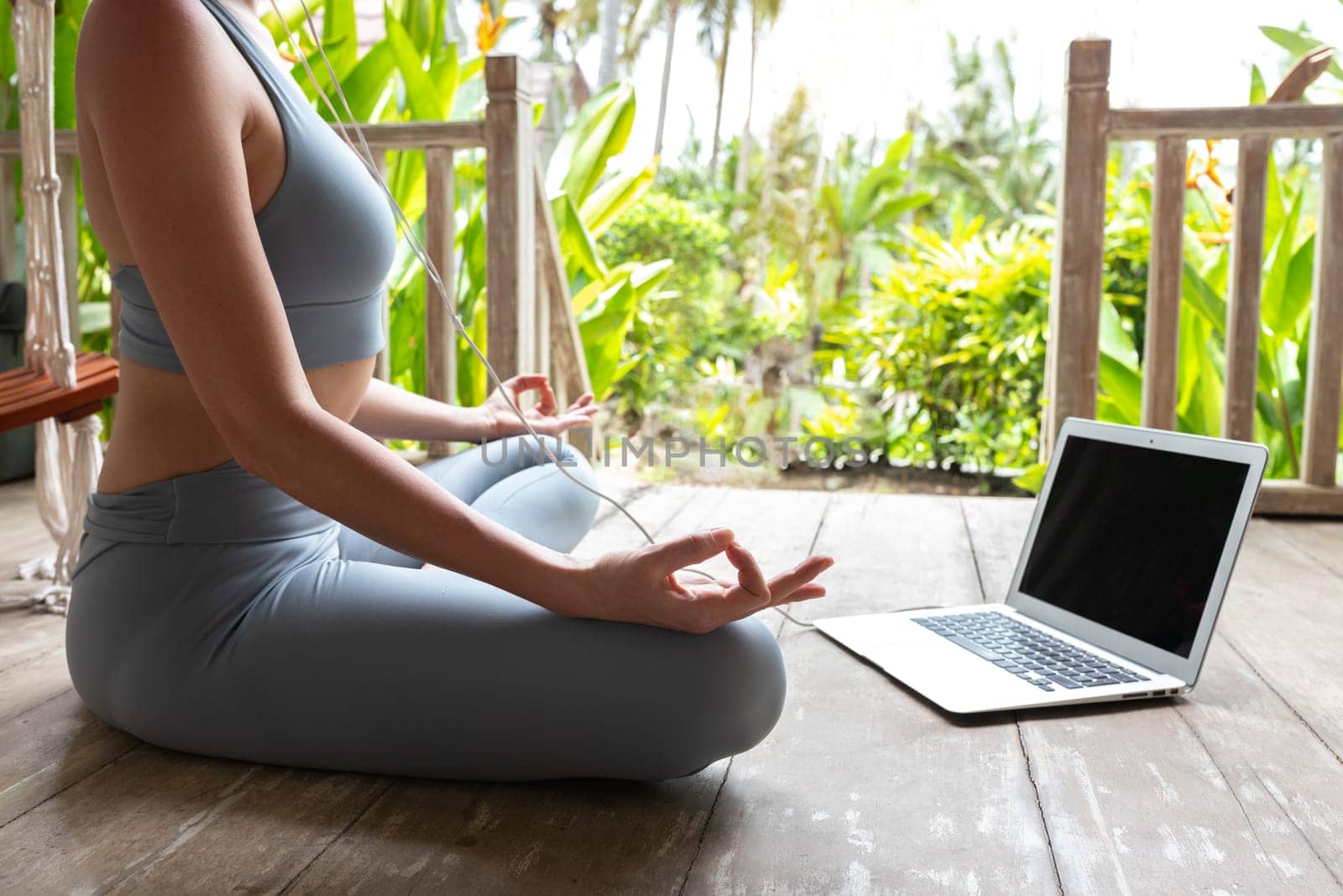 Unrecognizable woman in sports clothing following online meditation using laptop and headphones outdoors. by Hoverstock