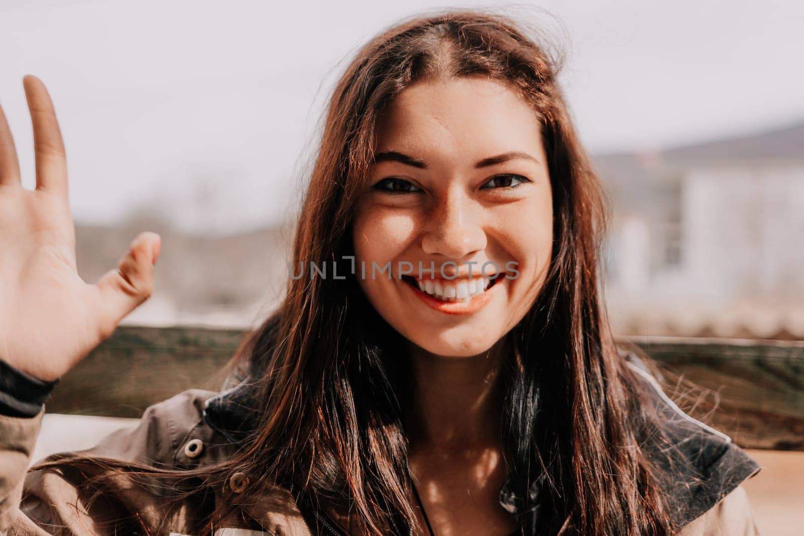 Happy young smiling woman with freckles outdoors portrait. Soft sunny colors. Outdoor close-up portrait of a young brunette woman and looking to the camera, posing against nature background.