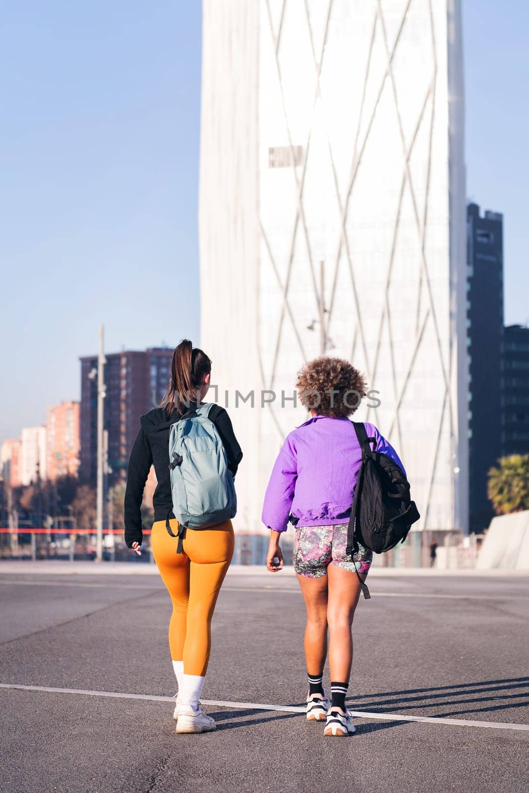 vertical photo with rear view of two women with sports clothes walking along the city, concept of friendship and urban sport