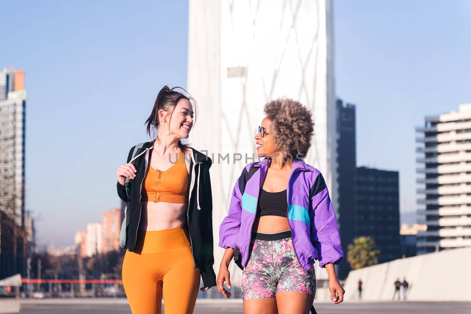 two women in sportswear talking while walking along the city, concept of friendship and urban sport, copy space for text