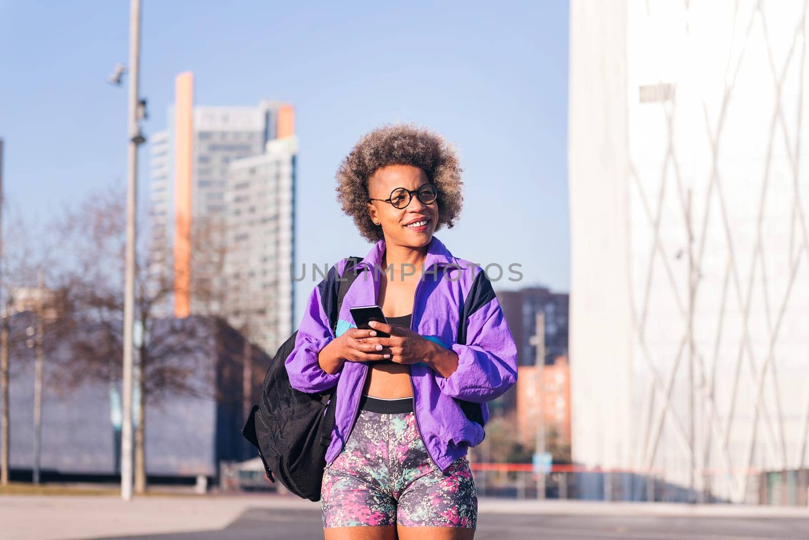african american woman in sports clothes using a mobile in the city, concept of technology of communication and urban sport, copy space for text