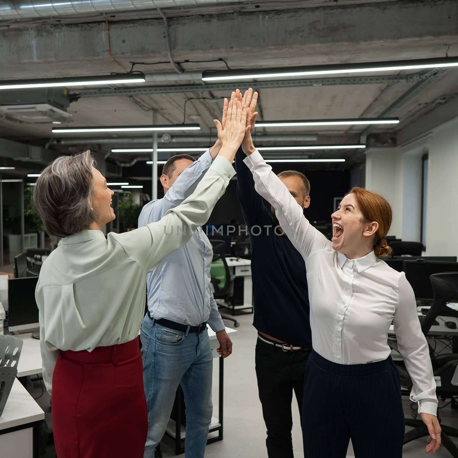 Four co-workers give a high five in the office. by mrwed54