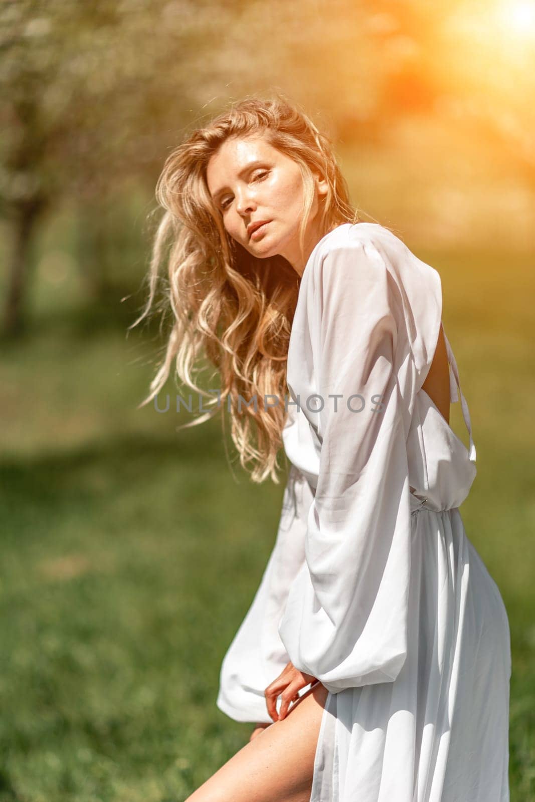 Blond blooming garden. A woman in a white dress walks through a blossoming cherry orchard. Long dress flies to the sides