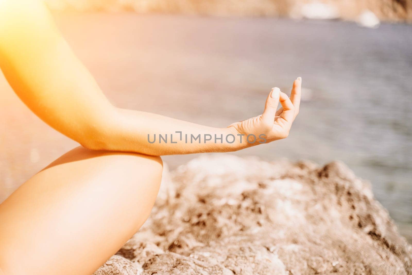 Yoga on the beach. A happy woman meditating in a yoga pose on the beach, surrounded by the ocean and rock mountains, promoting a healthy lifestyle outdoors in nature, and inspiring fitness concept