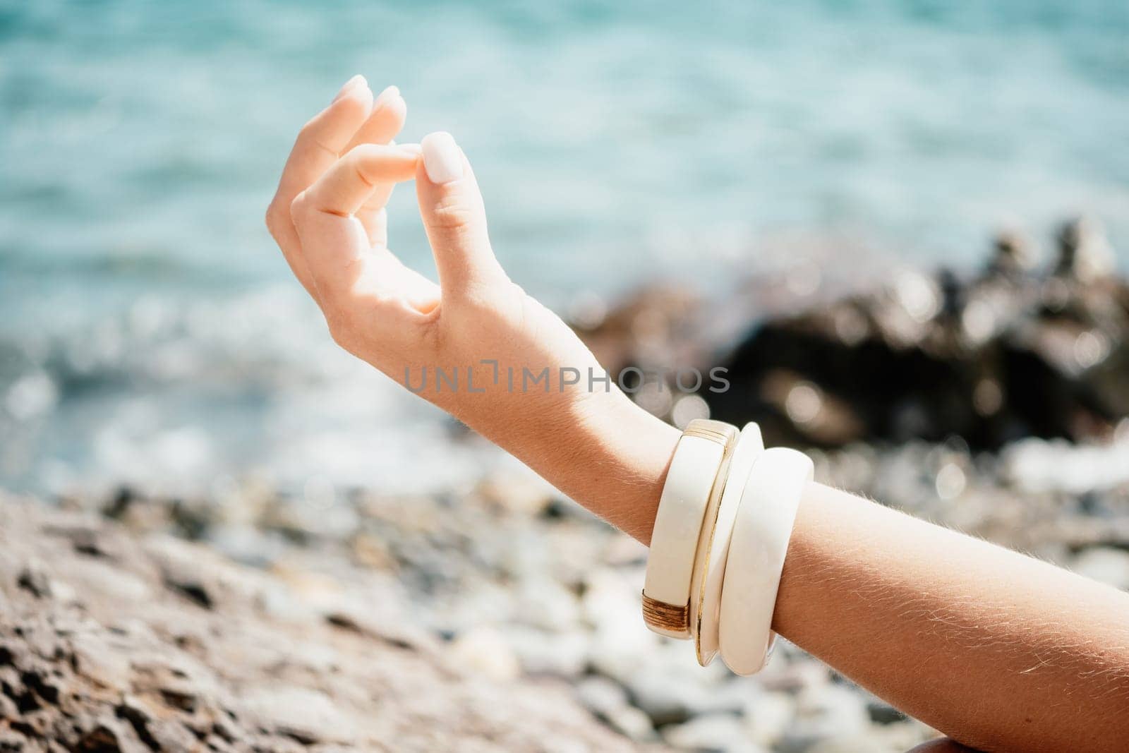 Close up Yoga Hand Gesture of Woman Doing an Outdoor meditation. Blurred sea background. Woman on yoga mat in beach meditation, mental health training or mind wellness by ocean, sea by panophotograph