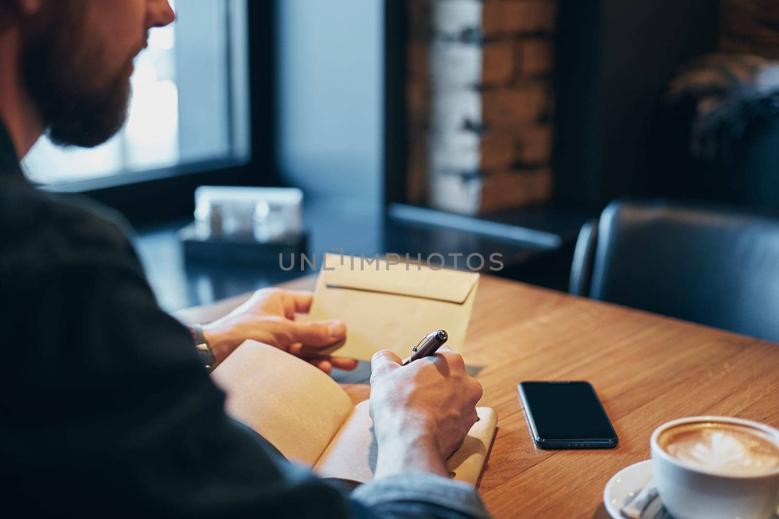 Man hand with pen writing on notebook on a wooden table. Man working at coffee shop. Close-up