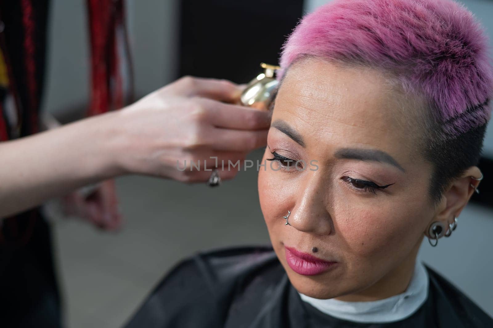 The hairdresser shaves the temple of a female client. Asian woman with short pink hair in barbershop. by mrwed54