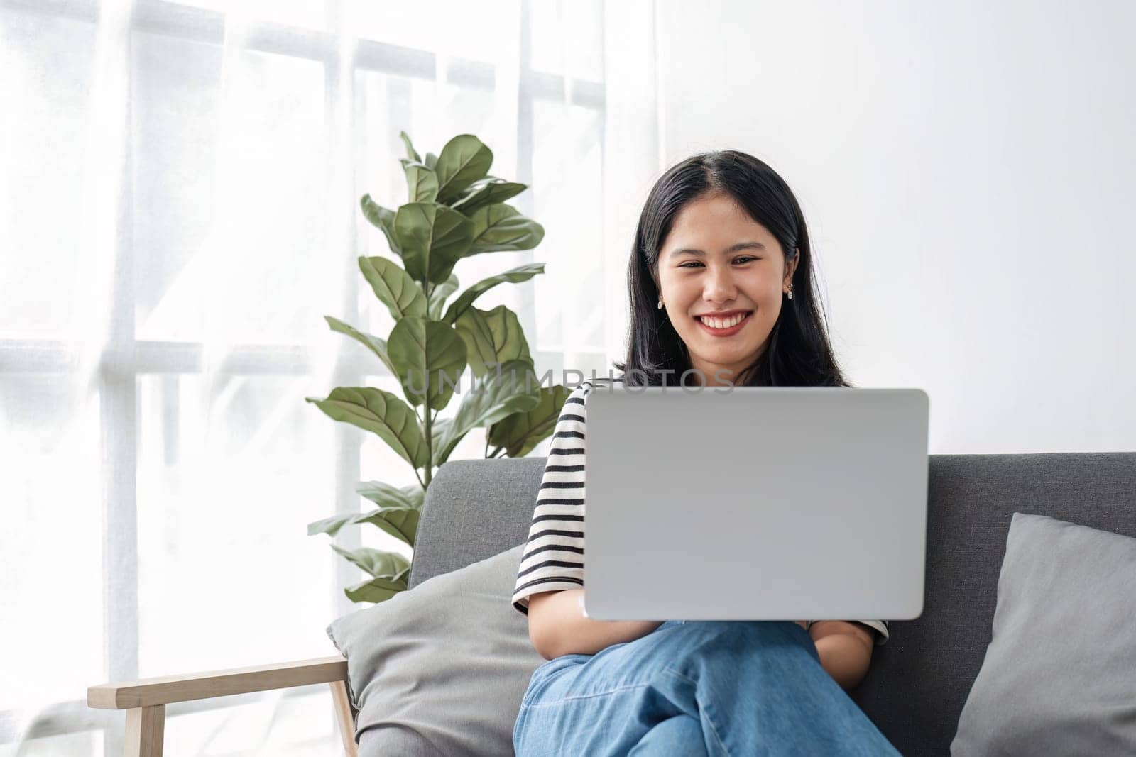 Young business freelance Asian woman working on laptop checking social media while lying on the sofa when relax in living room at home...