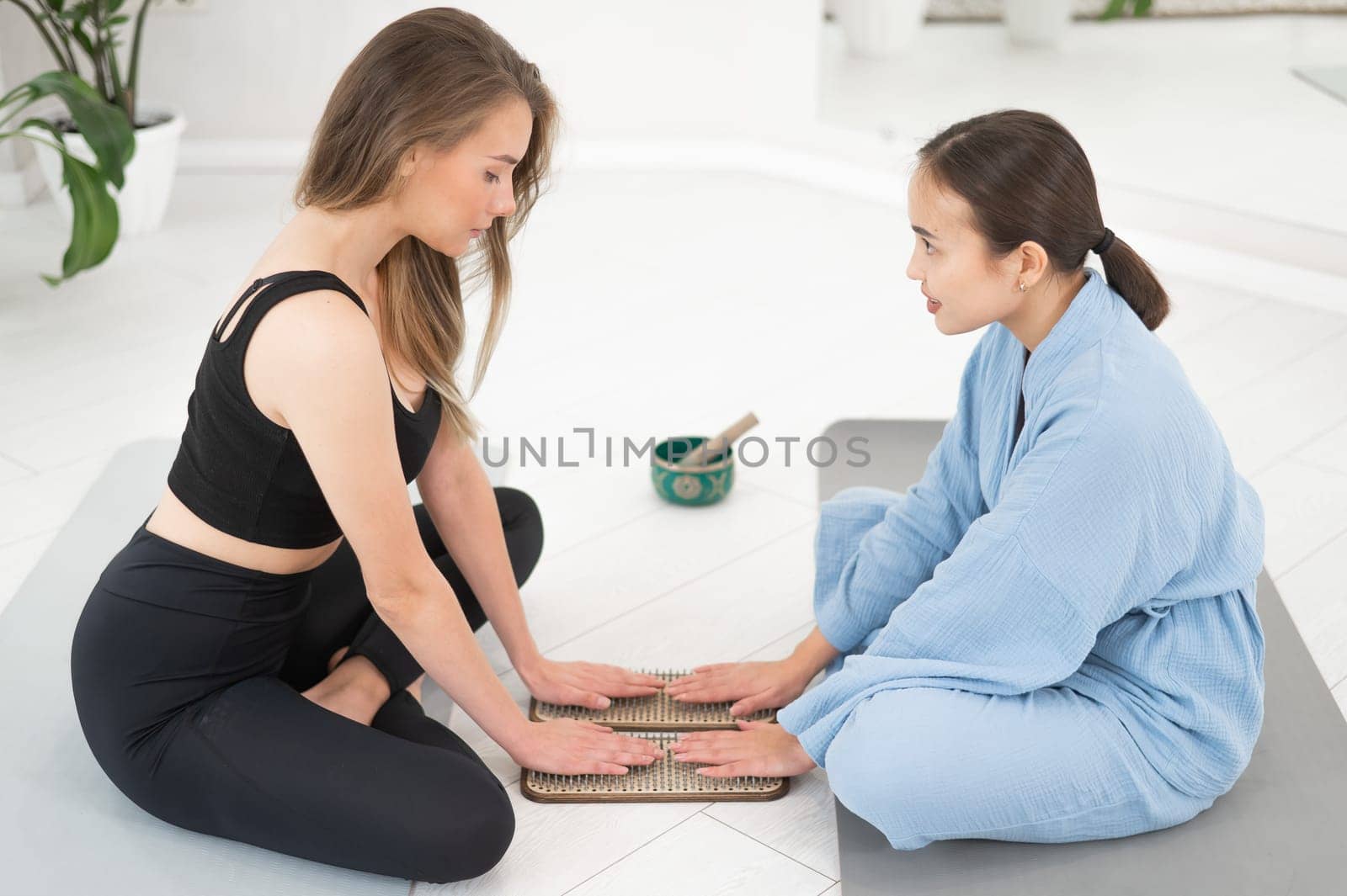 Two women sit on yoga mats with their hands on sadhu boards