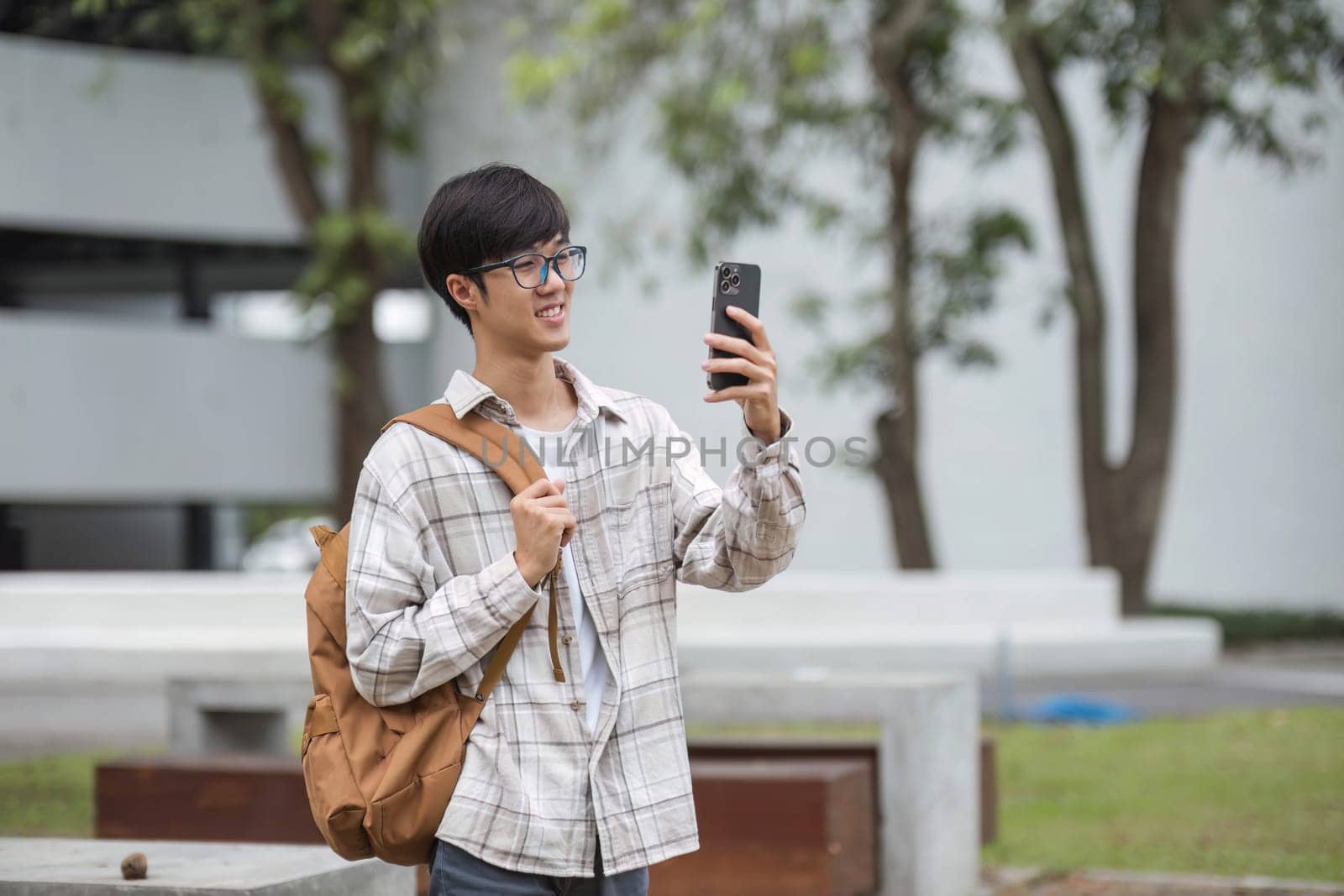 asian male college student with smart phone on sunny campus by wichayada