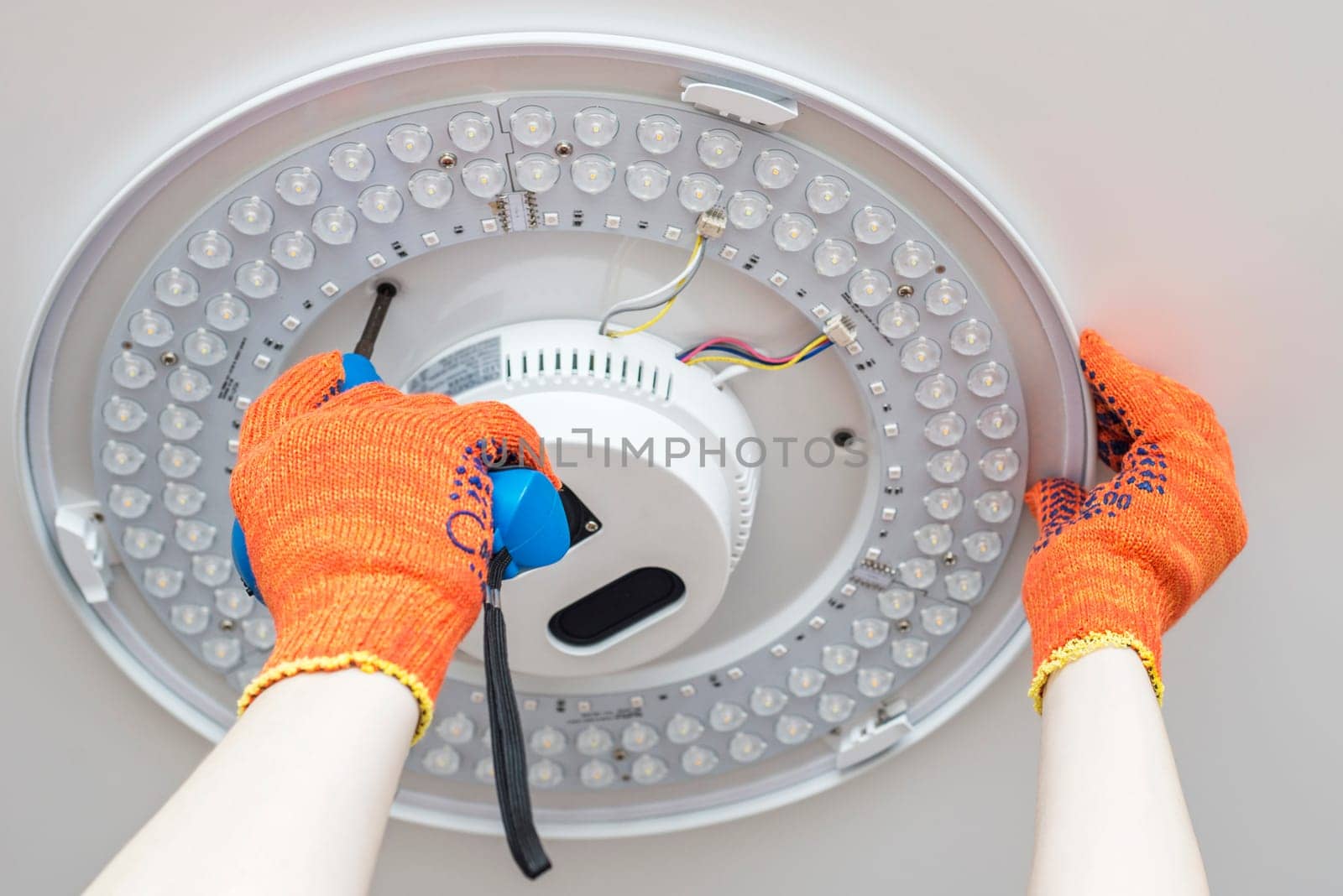 An electrician installs a chandelier on the ceiling. Hands of an electrician installing and connecting a lamp to a ceiling.