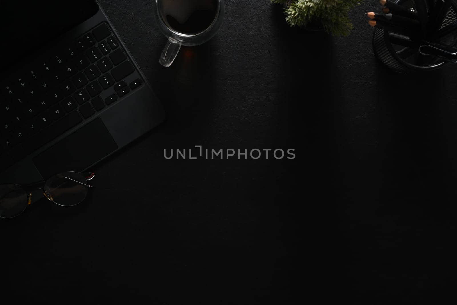 Dark modern workspace with laptop, notepad, coffee cup and glasses on black leather.