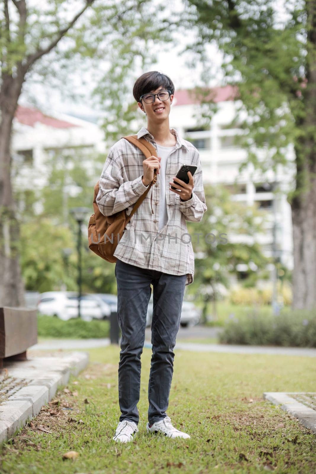 asian male college student with smart phone on sunny campus.