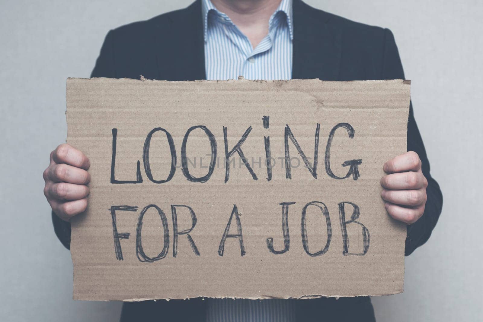 A young businessman who lost his job due to quarantine is looking for a job. A businessman holds a cardboard sign with the text LOOKING FOR A JOB. Unemployment growth concept