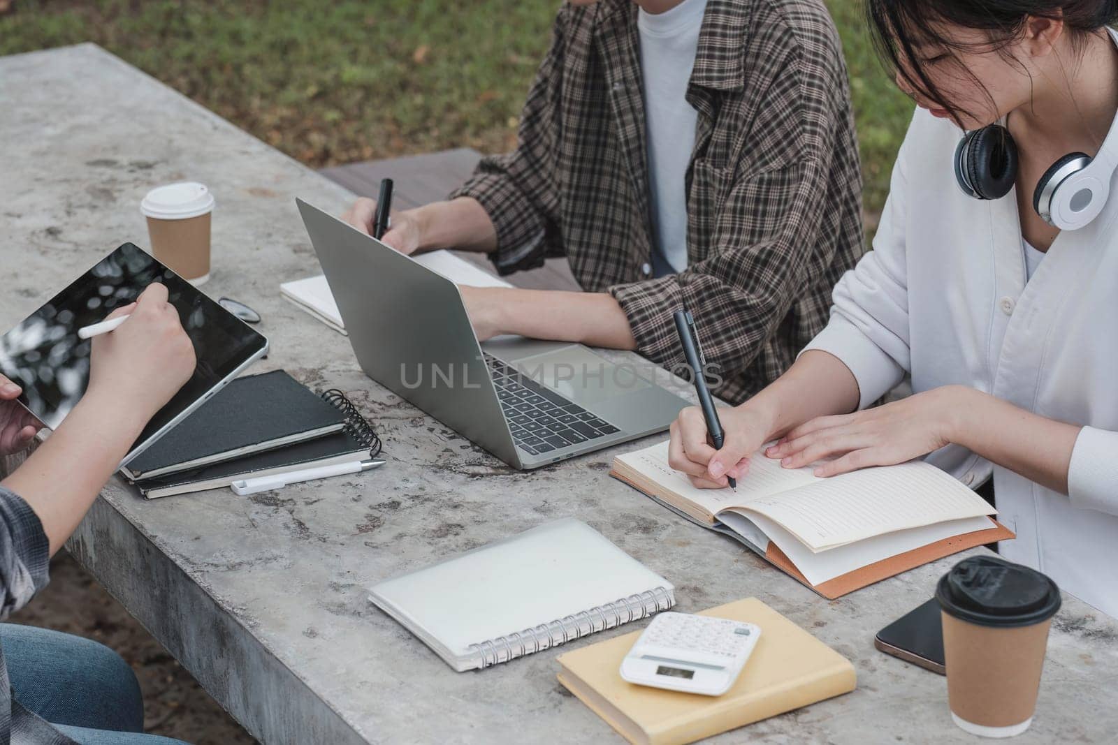 Group of Student working on laptop and record in book together at university. Happy friend successfully completes the thesis report and passed the final exam in asian college...