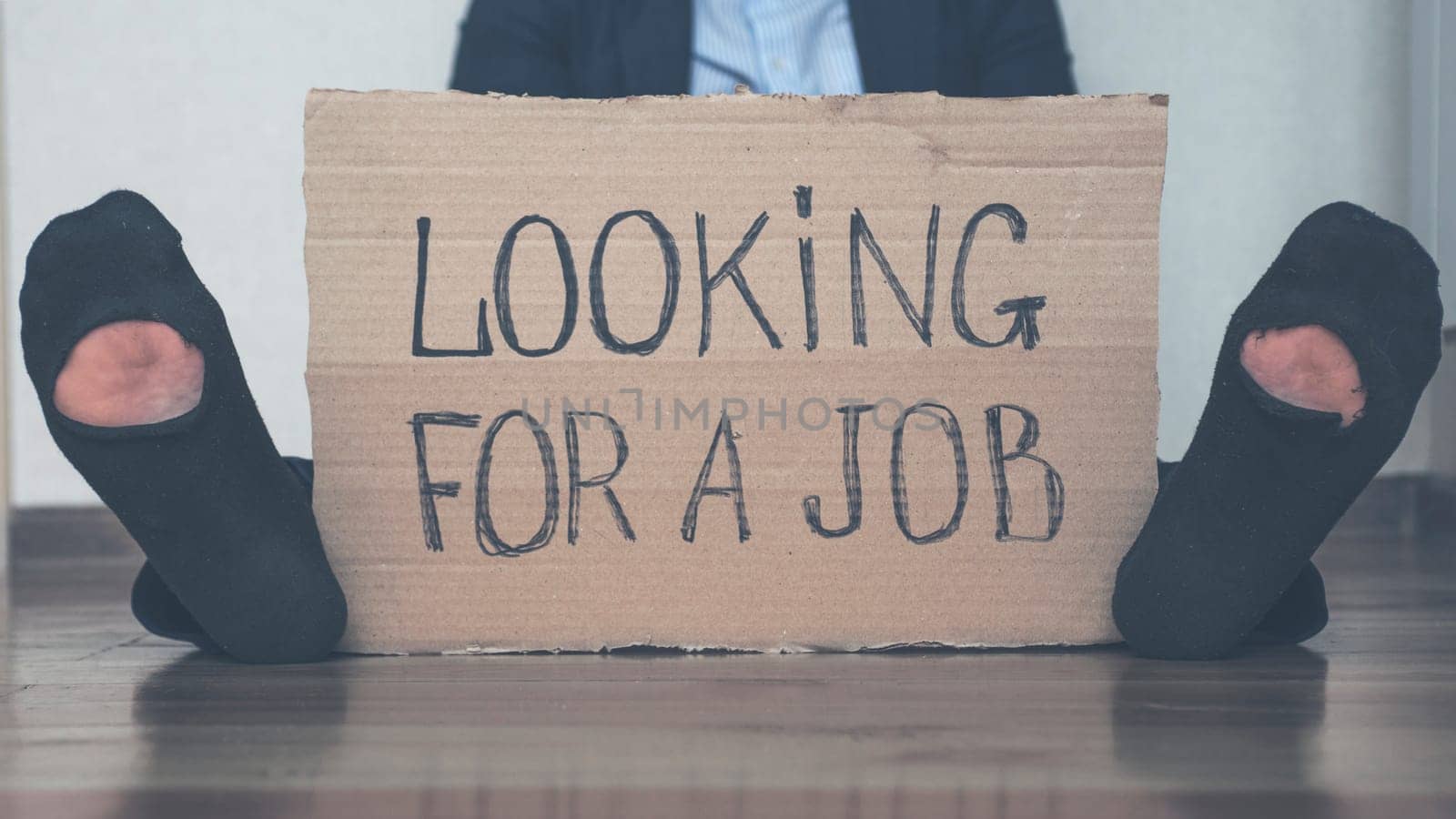 A young businessman who lost his job due to quarantine is looking for a job. A businessman sits on the floor with a cardboard sign with the text LOOKING FOR A JOB. Unemployment growth concept.