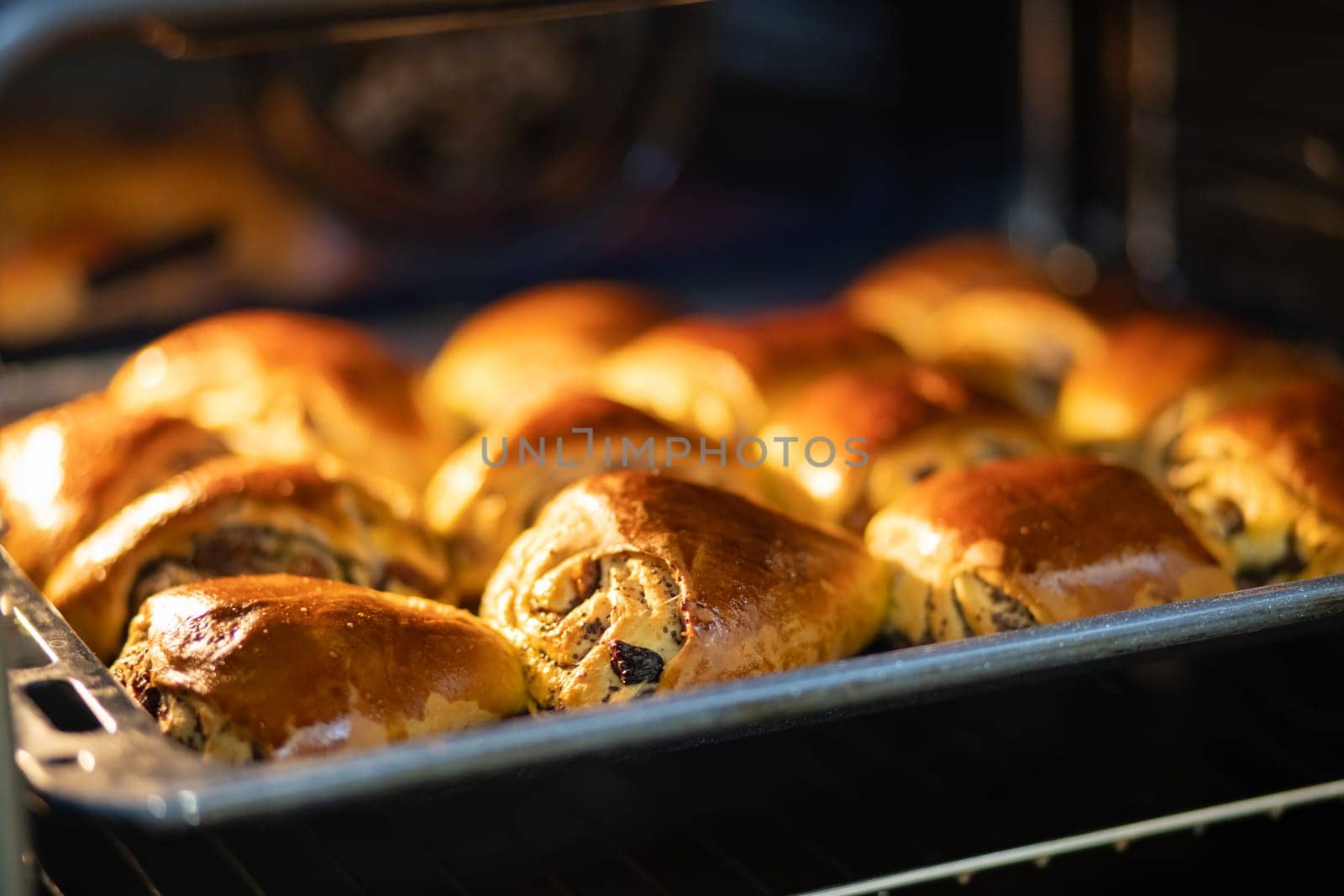 Buns baking in the oven. Freshly baked homemade buns with poppy seeds and raisins lie on a baking sheet.