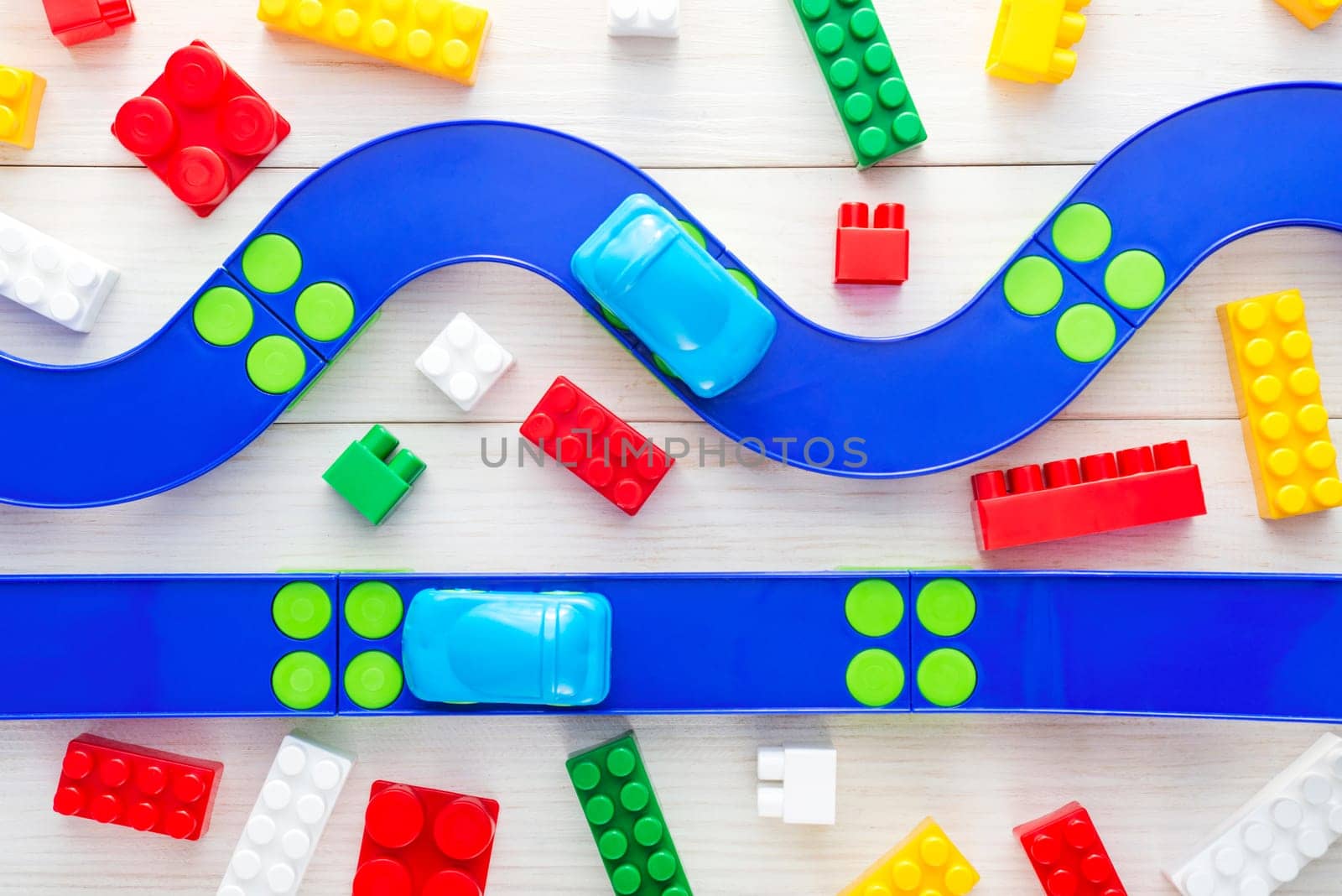 Baby kid toys background. Toy car, plastic road and colorful blocks on white wooden background. Top view.