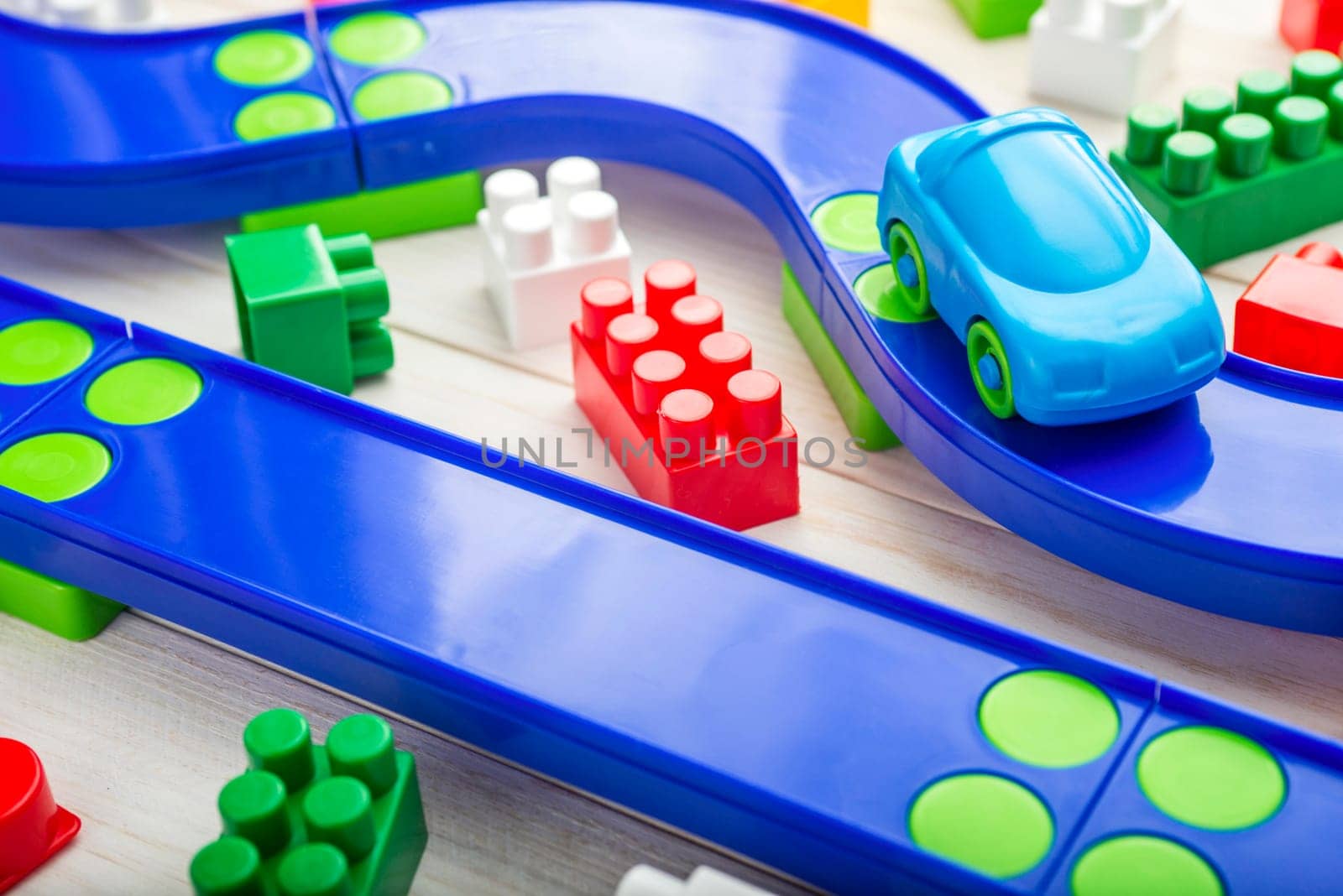 Baby kid toys background. Toy car, plastic road and colorful blocks on white wooden background.